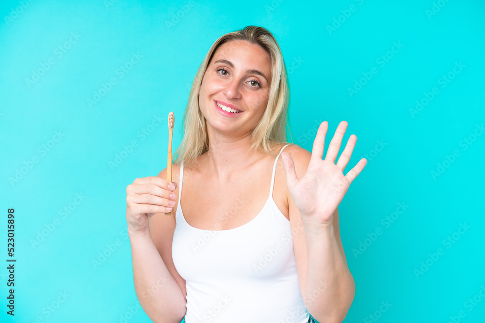 Young caucasian woman brushing teeth isolated on blue background saluting with hand with happy expression Young caucasian woman brushing teeth isolated on blue background saluting with hand with happy expression