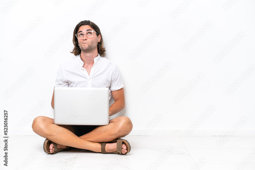 Young handsome man with a laptop sitting on the floor isolated on white background and looking up Young handsome man with a laptop sitting on the floor isolated on white background and looking up