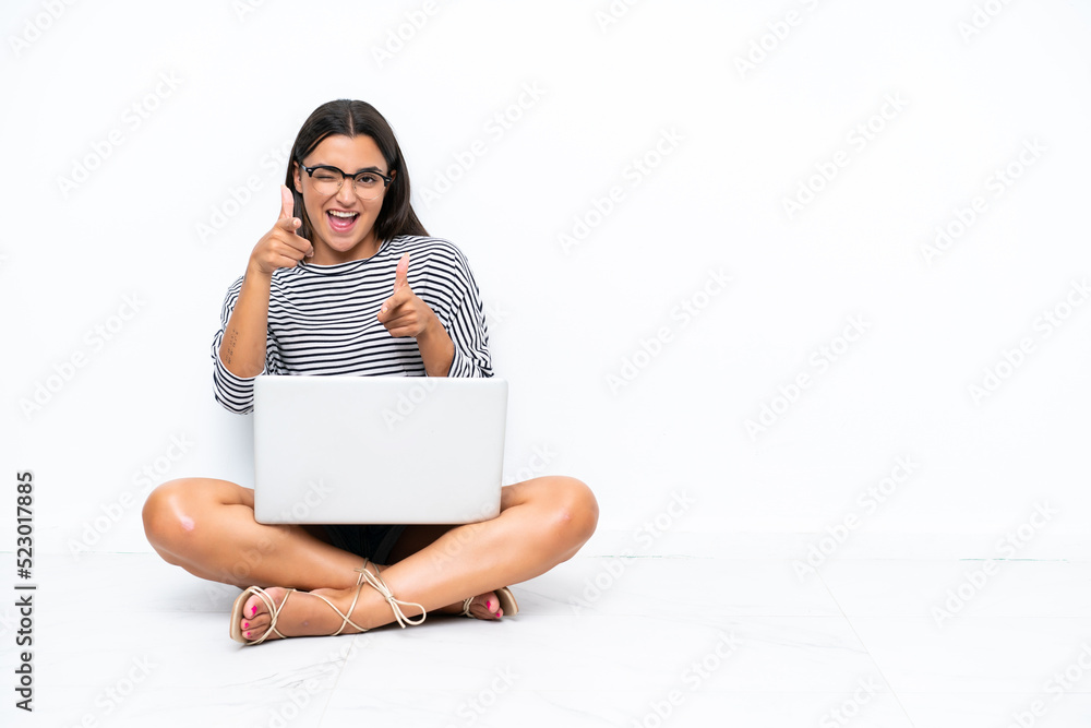 Young caucasian woman with a laptop sitting on the floor pointing to the front and smiling Young caucasian woman with a laptop sitting on the floor pointing to the front and smiling