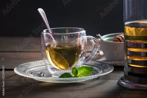 Herbal mint tea cup Transparent glass dark background wooden table still life honey bowl metal kettle teapot spoon cozy