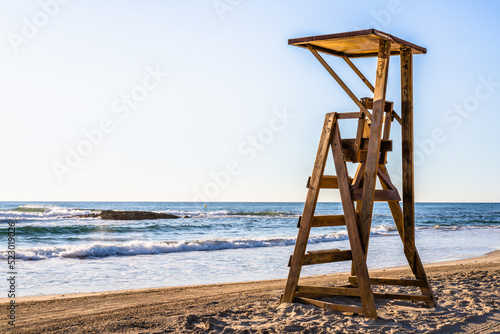 Mediterranean beach with wooden lifeguard chair in sunset time  in Spain. Teal and orange style.