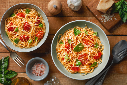 Plates of spaghetti with cherry tomatoes and fresh basil and ingredients on wooden background top view