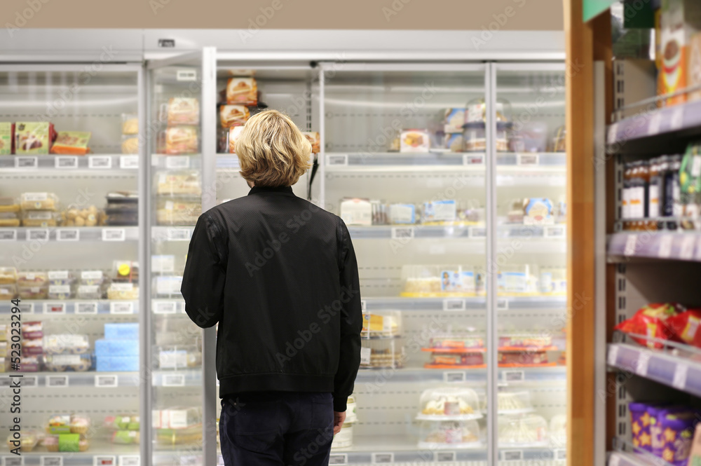  Man choosing frozen food from a supermarket freezer., reading product information