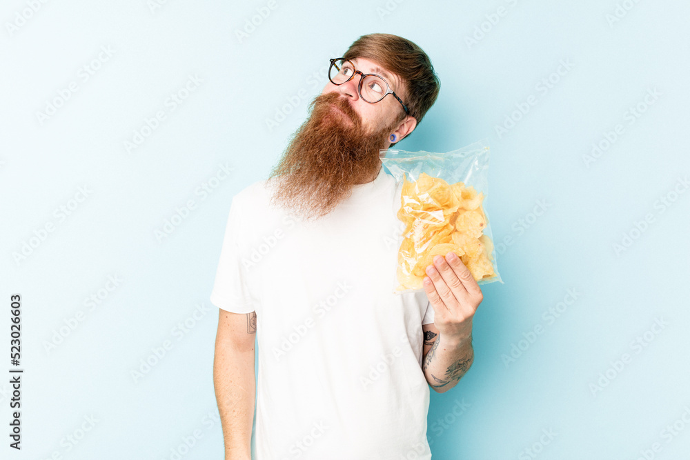Young caucasian man holding a bag of chips isolated on blue background dreaming of achieving goals and purposes Young caucasian man holding a bag of chips isolated on blue background dreaming of achieving goals and purposes