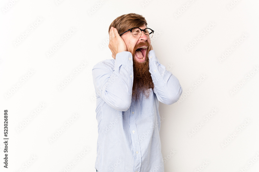Young caucasian red-haired man isolated on white background covering ears with hands trying not to hear too loud sound. Young caucasian red-haired man isolated on white background covering ears with hands trying not to hear too loud sound.
