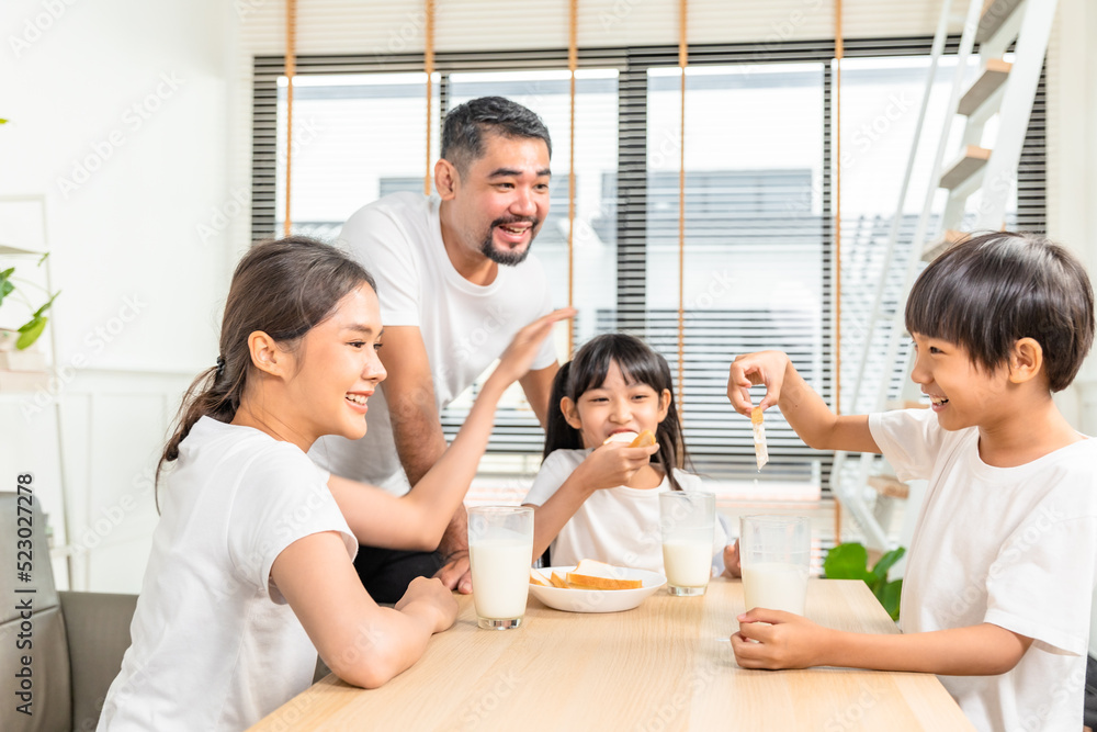 Asian family enjoying breakfast at living room. little girl daughter sitting on table, drinking milk with smiling father and mother in morning. Happy family at home. Asian family enjoying breakfast at living room. little girl daughter sitting on table, drinking milk with smiling father and mother in morning. Happy family at home.