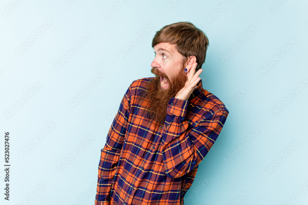 Young caucasian red-haired man isolated on blue background trying to listening a gossip. Young caucasian red-haired man isolated on blue background trying to listening a gossip.
