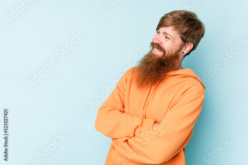 Young caucasian red-haired man isolated on blue background smiling confident with crossed arms.