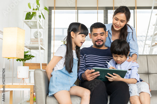 Asian family using tablet, laptop, phone for playing game or movies, relaxing at home for technology lifestyle concept.