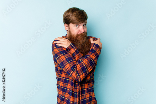 Young caucasian red-haired man isolated on blue background hugs, smiling carefree and happy.