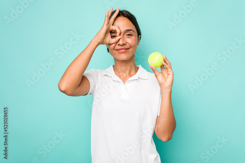 Young hispanic physiotherapy holding a tennis ball isolated on blue background excited keeping ok gesture on eye. © Asier