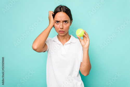 Young hispanic physiotherapy holding a tennis ball isolated on blue background being shocked, she has remembered important meeting. © Asier