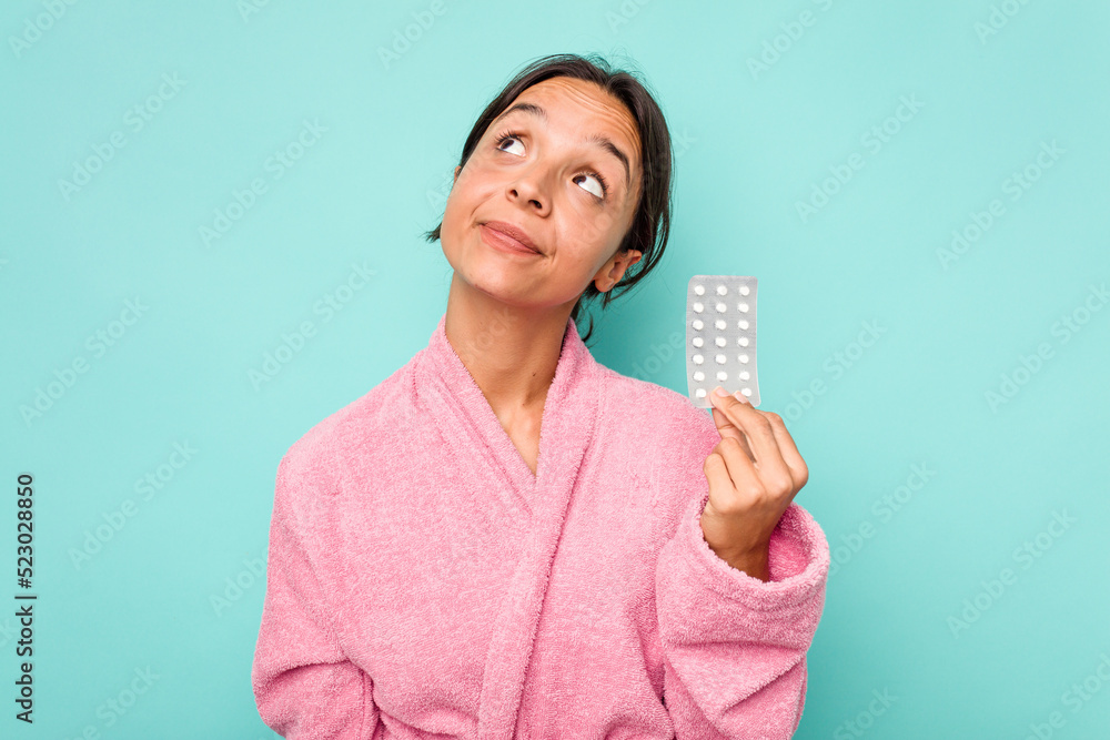 Young hispanic woman holding pills isolated on blue background dreaming of achieving goals and purposes Young hispanic woman holding pills isolated on blue background dreaming of achieving goals and purposes