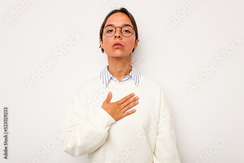 Young hispanic woman isolated on white background taking an oath, putting hand on chest. © Asier