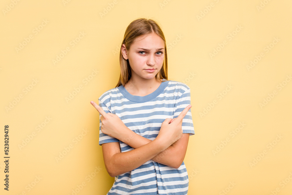 Young caucasian girl isolated on yellow background points sideways, is trying to choose between two options. Young caucasian girl isolated on yellow background points sideways, is trying to choose between two options.