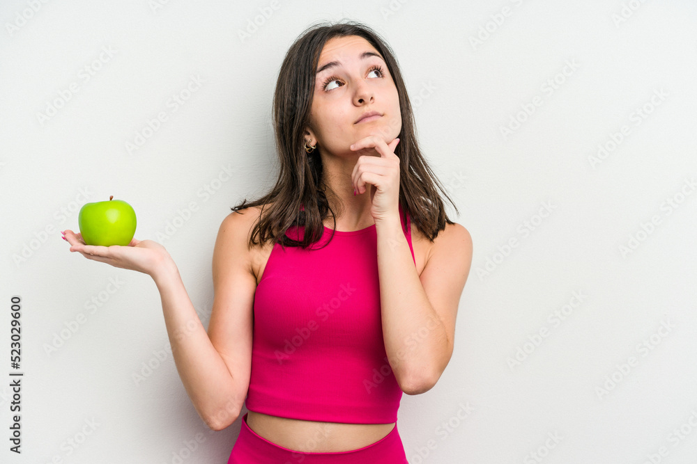 Young caucasian woman holding an apple isolated on white background looking sideways with doubtful and skeptical expression. Young caucasian woman holding an apple isolated on white background looking sideways with doubtful and skeptical expression.