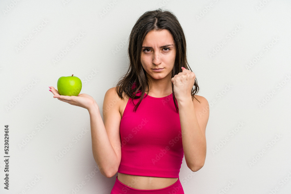 Young caucasian woman holding an apple isolated on white background showing fist to camera, aggressive facial expression. Young caucasian woman holding an apple isolated on white background showing fist to camera, aggressive facial expression.