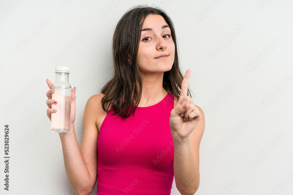 Young caucasian woman holding a bottle of water isolated on white background showing number one with finger. Young caucasian woman holding a bottle of water isolated on white background showing number one with finger.
