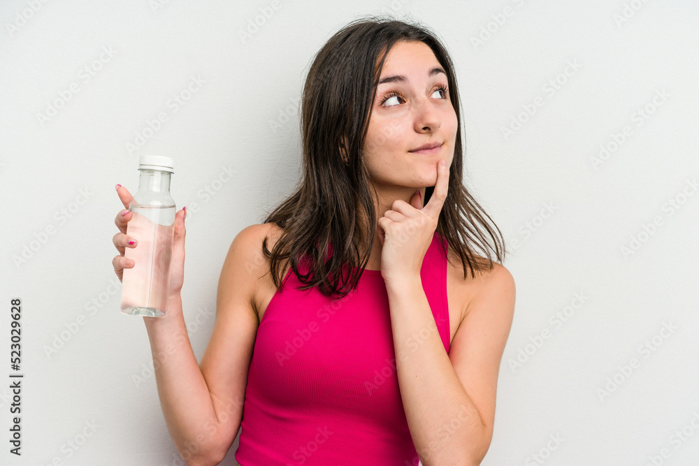 Young caucasian woman holding a bottle of water isolated on white background relaxed thinking about something looking at a copy space. Young caucasian woman holding a bottle of water isolated on white background relaxed thinking about something looking at a copy space.