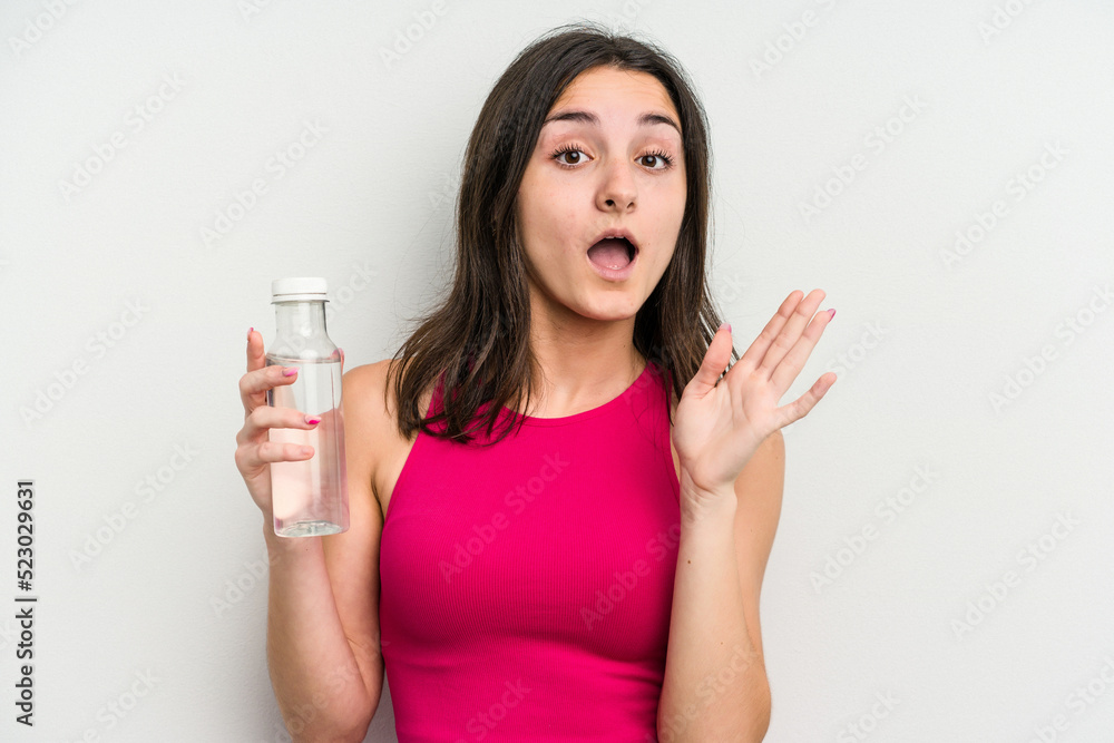 Young caucasian woman holding a bottle of water isolated on white background surprised and shocked. Young caucasian woman holding a bottle of water isolated on white background surprised and shocked.