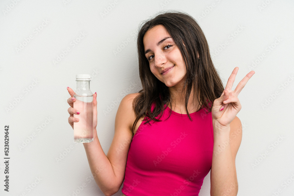 Young caucasian woman holding a bottle of water isolated on white background joyful and carefree showing a peace symbol with fingers. Young caucasian woman holding a bottle of water isolated on white background joyful and carefree showing a peace symbol with fingers.