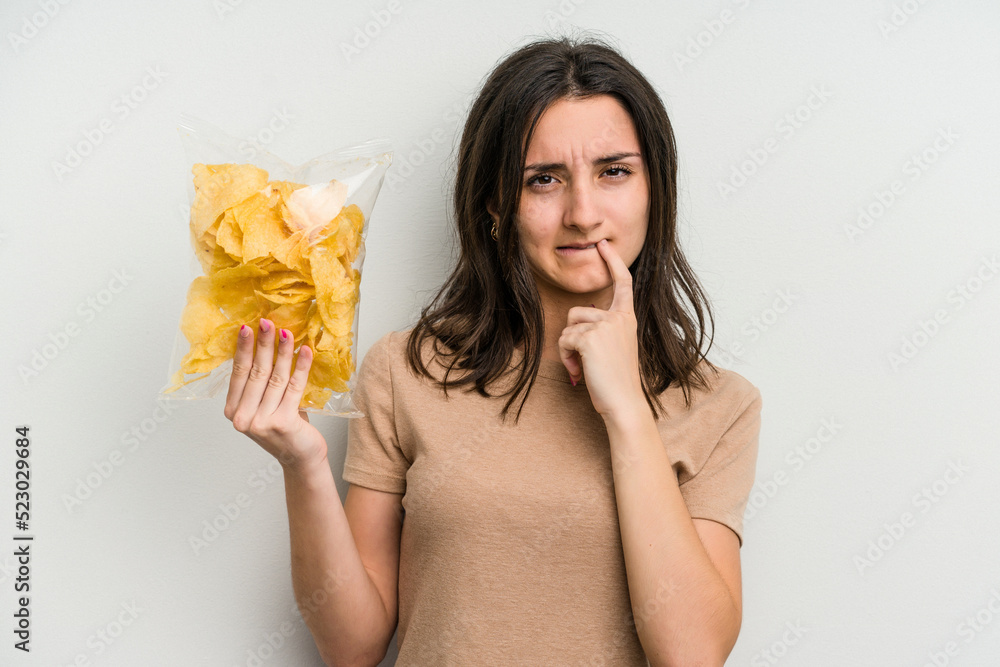 Young caucasian woman holding crisps isolated on yellow background biting fingernails, nervous and very anxious. Young caucasian woman holding crisps isolated on yellow background biting fingernails, nervous and very anxious.