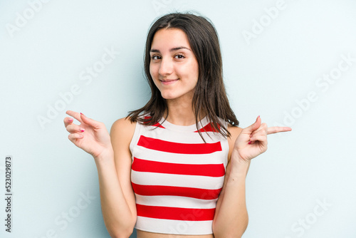 Young caucasian woman isolated on blue background pointing to different copy spaces, choosing one of them, showing with finger.