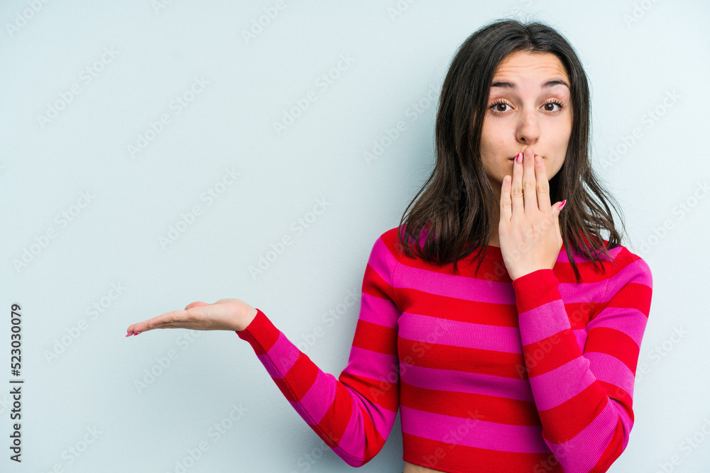 Young caucasian woman isolated on blue background impressed holding copy space on palm. Young caucasian woman isolated on blue background impressed holding copy space on palm.