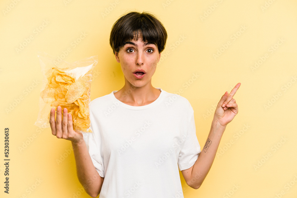 Young caucasian man holding crisps isolated on yellow background pointing to the side Young caucasian man holding crisps isolated on yellow background pointing to the side