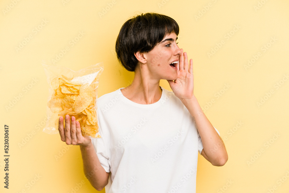 Young caucasian man holding crisps isolated on yellow background shouting and holding palm near opened mouth. Young caucasian man holding crisps isolated on yellow background shouting and holding palm near opened mouth.