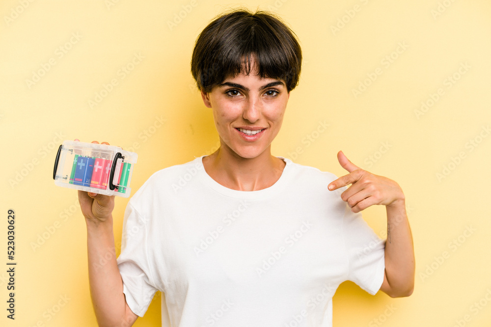 Young caucasian woman holding a batteries box isolated on yellow background person pointing by hand to a shirt copy space, proud and confident Young caucasian woman holding a batteries box isolated on yellow background person pointing by hand to a shirt copy space, proud and confident