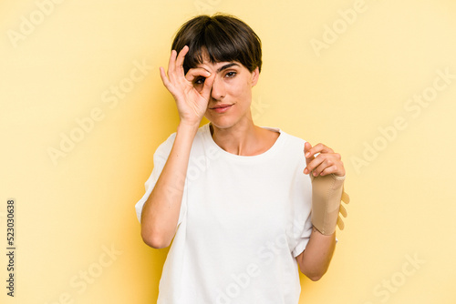 Young caucasian woman hand sling isolated on yellow background excited keeping ok gesture on eye.