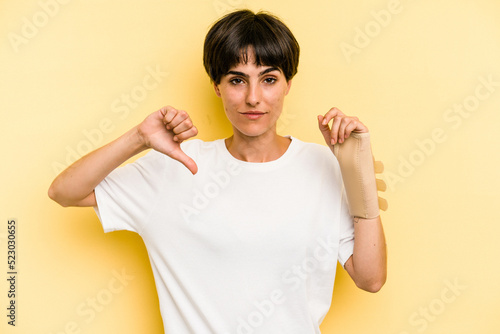 Young caucasian woman hand sling isolated on yellow background showing a dislike gesture, thumbs down. Disagreement concept.