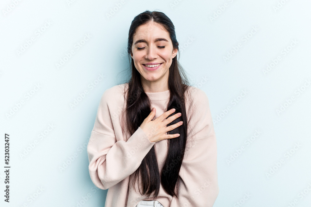 Young caucasian woman isolated on blue background laughs out loudly keeping hand on chest. Young caucasian woman isolated on blue background laughs out loudly keeping hand on chest.