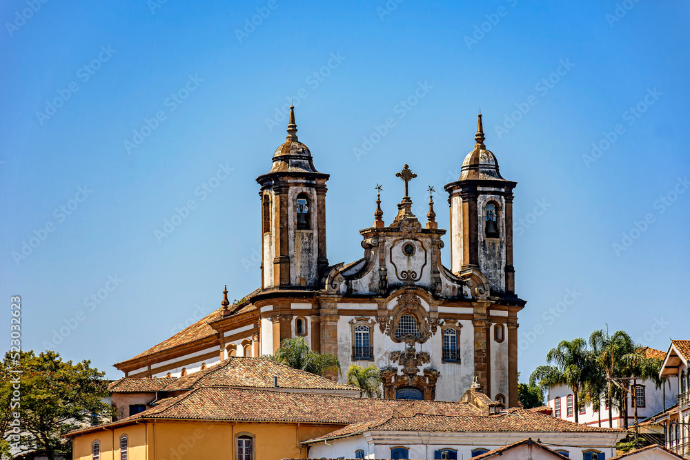 Baroque style historic church tower emerging from behind old houses in Ouro Preto city in Minas Gerais state, Brazil