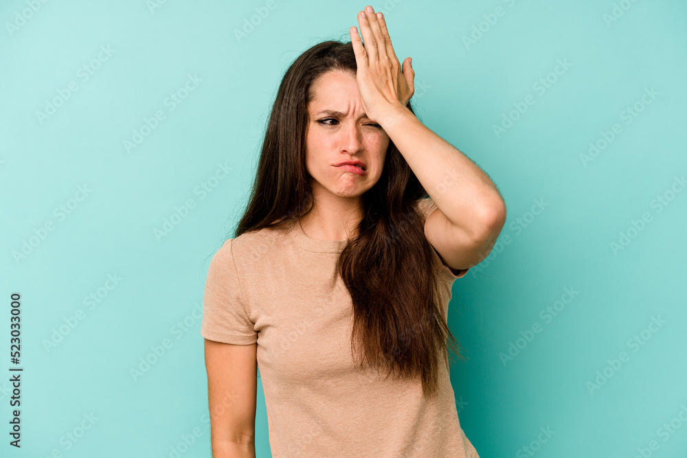 Young caucasian woman isolated on blue background forgetting something, slapping forehead with palm and closing eyes.