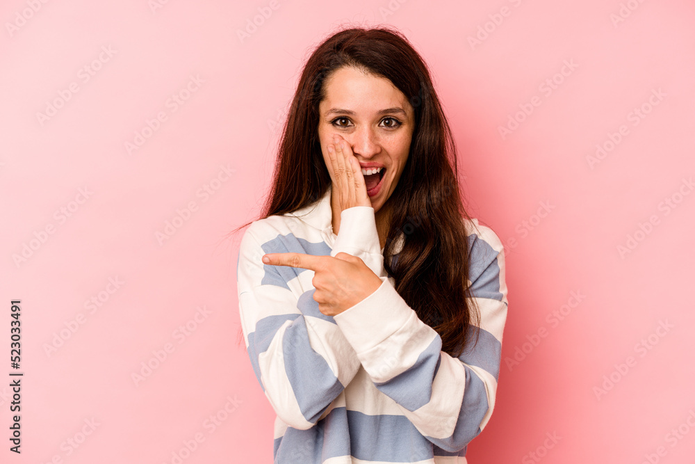 Young caucasian woman isolated on pink background saying a gossip, pointing to side reporting something. Young caucasian woman isolated on pink background saying a gossip, pointing to side reporting something.