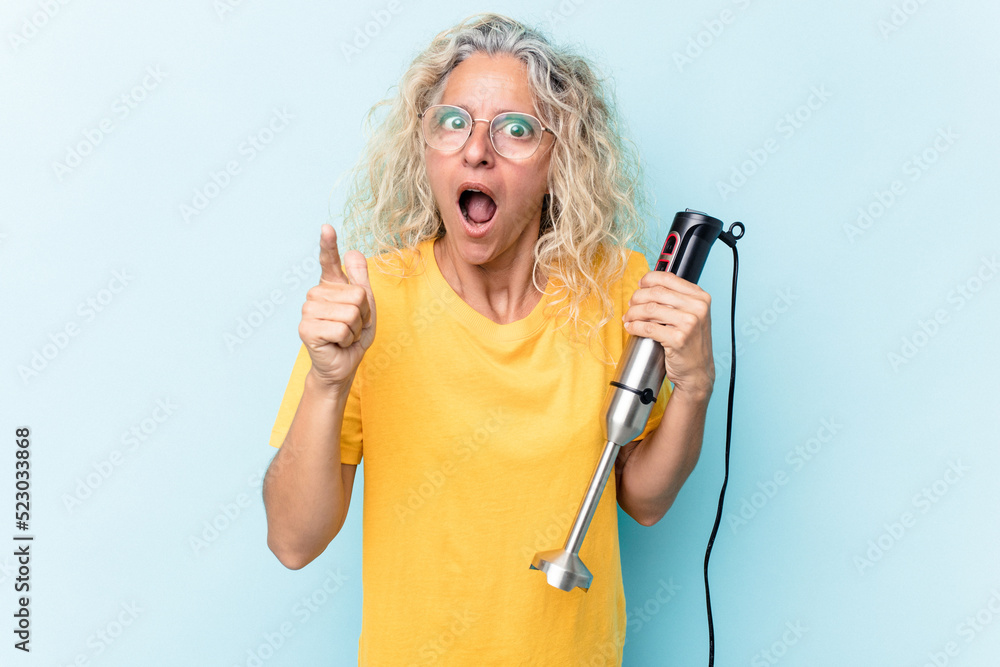 Middle age woman holding a blender isolated on blue background having an idea, inspiration concept. Middle age woman holding a blender isolated on blue background having an idea, inspiration concept.