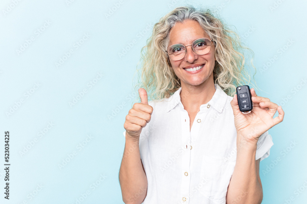 Middle age caucasian woman holding a car keys isolated on blue background smiling and raising thumb up Middle age caucasian woman holding a car keys isolated on blue background smiling and raising thumb up