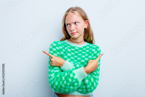Caucasian teen girl isolated on blue background points sideways, is trying to choose between two options.