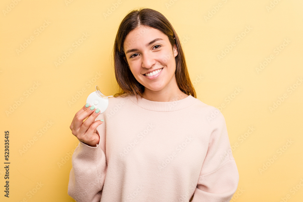 Young caucasian woman holding teeth whitener isolated on yellow background happy, smiling and cheerful. Young caucasian woman holding teeth whitener isolated on yellow background happy, smiling and cheerful.