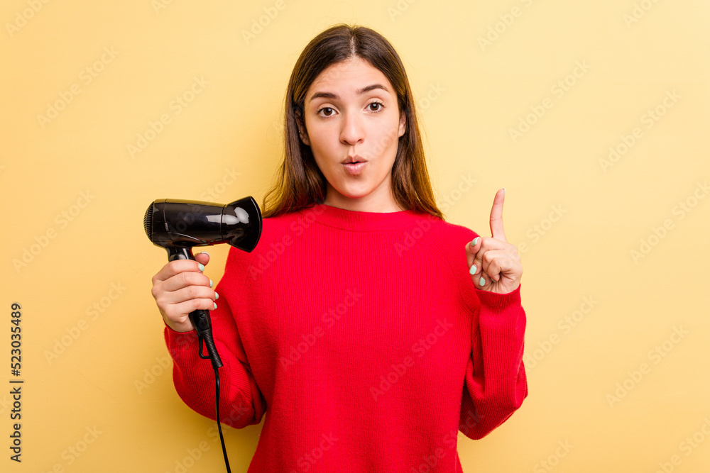 Young caucasian woman holding hairdryer isolated on yellow background having some great idea, concept of creativity. Young caucasian woman holding hairdryer isolated on yellow background having some great idea, concept of creativity.