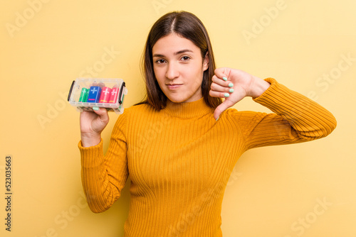 Young caucasian woman holding a batteries box isolated on yellow background showing a dislike gesture  thumbs down. Disagreement concept.