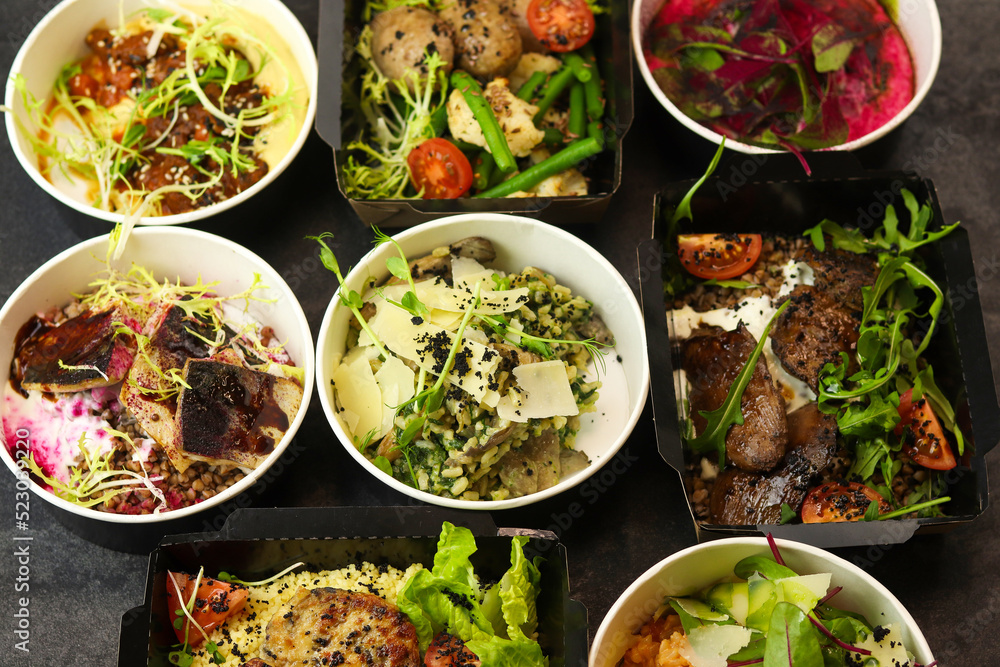 Delivery of healthy food in takeaway restaurants for daily nutrition. Set of containers with everyday meals - meat, fish, vegetables and law fat snacks on a black background. Delivery of healthy food in takeaway restaurants for daily nutrition. Set of containers with everyday meals - meat, fish, vegetables and law fat snacks on a black background.