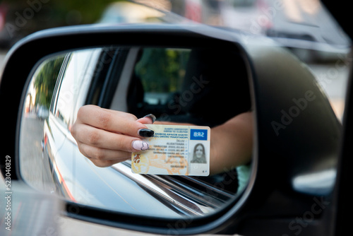 Teenager girl showing his driver's license in the car window after passing the exam or at the request of the traffic police