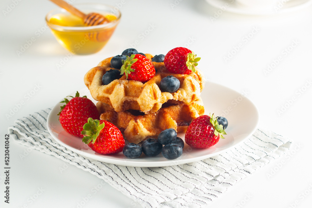 Fresh homemade food of berry Belgian waffles with honey, chocolate, strawberry, blueberry, maple syrup and cream. Healthy dessert breakfast concept with coffee Fresh homemade food of berry Belgian waffles with honey, chocolate, strawberry, blueberry, maple syrup and cream. Healthy dessert breakfast concept with coffee