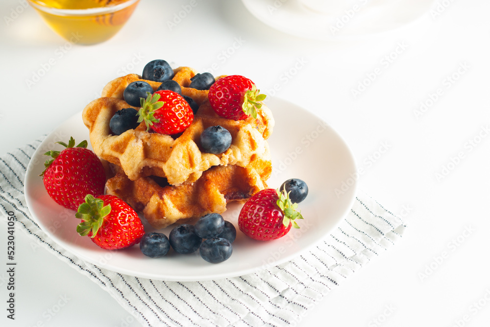 Fresh homemade food of berry Belgian waffles with honey, chocolate, strawberry, blueberry, maple syrup and cream. Healthy dessert breakfast concept with coffee Fresh homemade food of berry Belgian waffles with honey, chocolate, strawberry, blueberry, maple syrup and cream. Healthy dessert breakfast concept with coffee