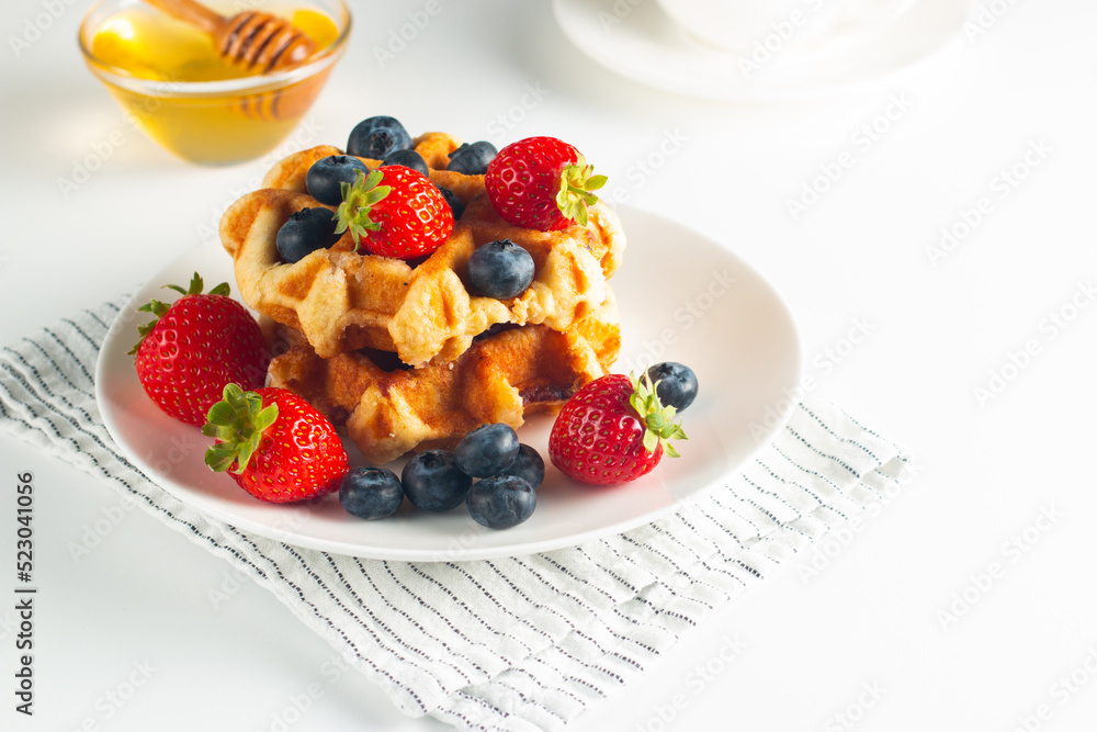 Fresh homemade food of berry Belgian waffles with honey, chocolate, strawberry, blueberry, maple syrup and cream. Healthy dessert breakfast concept with coffee Fresh homemade food of berry Belgian waffles with honey, chocolate, strawberry, blueberry, maple syrup and cream. Healthy dessert breakfast concept with coffee