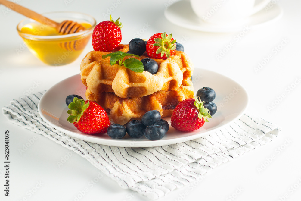 Fresh homemade food of berry Belgian waffles with honey, chocolate, strawberry, blueberry, maple syrup and cream. Healthy dessert breakfast concept with coffee Fresh homemade food of berry Belgian waffles with honey, chocolate, strawberry, blueberry, maple syrup and cream. Healthy dessert breakfast concept with coffee