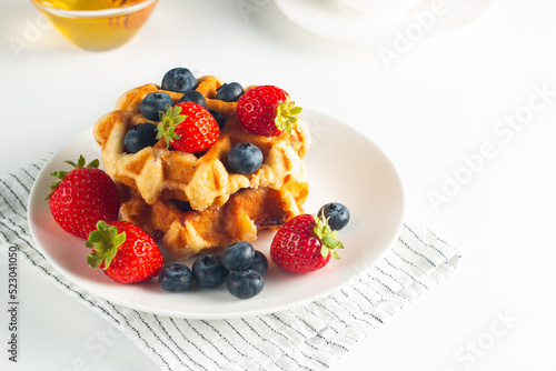 Fresh homemade food of berry Belgian waffles with honey  chocolate  strawberry  blueberry  maple syrup and cream. Healthy dessert breakfast concept with coffee